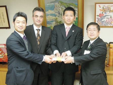 左から木戸雅之社長、ブラシオスヘッドコーチ、沢口誠選手、市長と並び寄贈されたチケットの入れ物を持ち記念撮影している写真