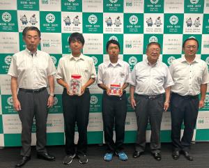 義援金を入れた募金箱を持った2人の生徒と市長ら関係者3名が並んでいる写真