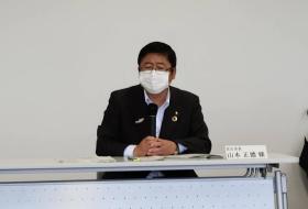 マスク姿の市長が自席で座って、両手でマイクを持ちながら意見を述べている写真