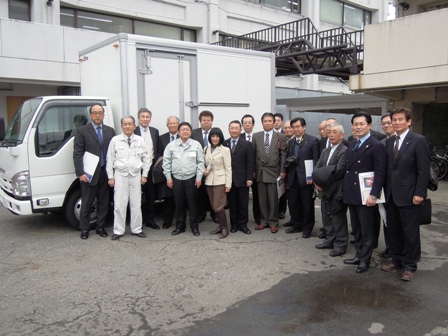 白色の車体のトラックの前でスーツや作業着をきた関係者の方々と市長が並び記念撮影している写真
