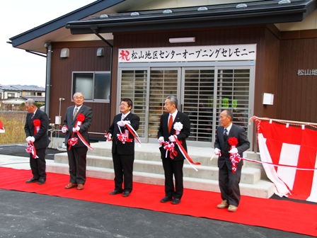 入口上に「祝 松山地区センターオープニングセレモニー」の横断幕が飾られており、建物前に敷かれた赤じゅうたんの上に市長と関係者が並んでおり、テープカットをした写真
