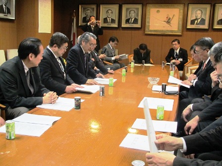 長机に資料が置かれており、向かい合って座る市長と関係者達の写真