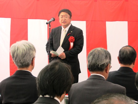 紅白幕の前に置かれたスタンドマイクに向かい話をする市長と、椅子に座り整列する関係者の方々の写真