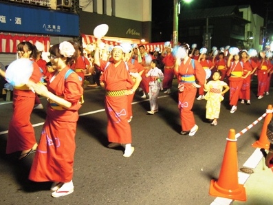 真っ赤な浴衣をきた方達が道路の真ん中で団扇を持ちながら踊っている写真