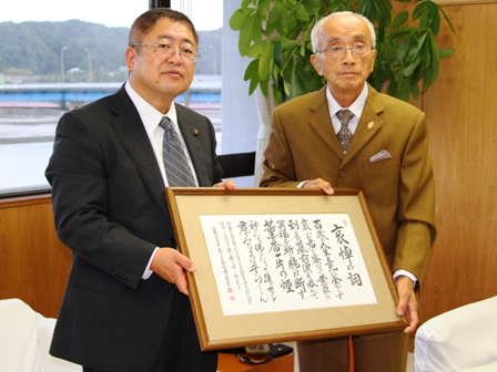 筆字で書かれた書の額縁を、市長と馬場英男さんが一緒に手に持っている写真