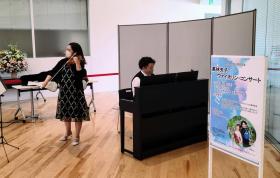 施設内の一角にパーティションなどで設営した会場で佐藤慎吾さんのピアノの伴奏に合わせて、高林央子さんがバイオリンの演奏をしている写真