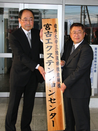 縦書きで「宮古エクステンションセンター」と書かれた一枚板の木製看板を市長と男性が二人で手に持っている写真