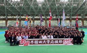 「歓迎 早稲田大学応援部」と書かれた横断幕の後方で、関係者の応援部の学生たちが集合して記念撮影をしている写真