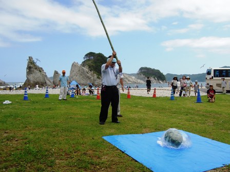 浄土ヶ浜海水浴場の芝生の上で、2メートルほどの長い竹竿を両手に構え、目隠しをした市長が、ビニールシートの上に置かれたすいかに向かって歩いている写真