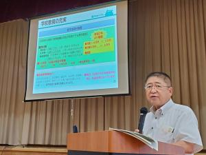 画面が映されたスクリーンの斜め前の演台で、マイクを手に持ち話をする様子の市長の写真