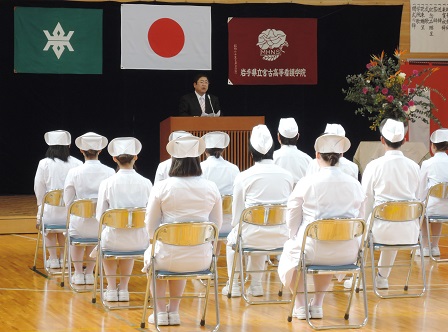 パイプ椅子に座った白い制服とナースキャップを被った看護学生たちと、演台のマイクに向かい話をする市長が写った写真