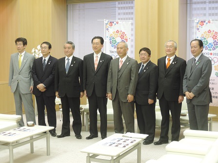 横一列に並ぶ市長、舛添要一都知事、6名の関係者の男性の記念写真