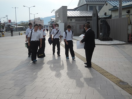 道を歩く学生たちに、パネルを見せながら話しかけている市長の写真