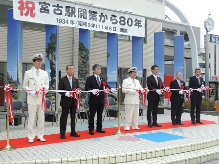 白い制帽と制服を身に着けた市長と男性1名、スーツを着た男性5名が横一列に並びテープカットをしている様子の写真