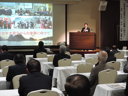 画面が映されたスクリーンの横に置かれた演台のマイクに向かい話をする様子の市長の写真