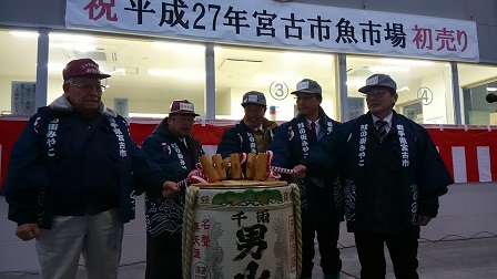 宮古市魚市場初売りの横断幕と紅白の幕が施された市場の前で、帽子を被り法被を着た市長の他、4人で酒樽を鏡開きしている写真