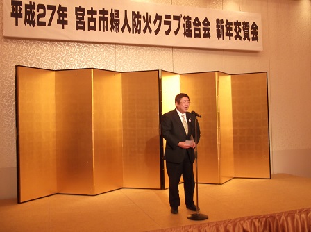 宮古市婦人防火クラブ連合会新年交賀会と書かれた横断幕がある ステージの金屛風の前で、市長があいさつを述べている写真