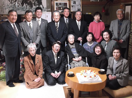 座っている中屋ハナさんの前の円卓のちゃぶ台にお祝いのケーキが置かれ、中屋ハナさんを 中心にして、市長の他、13名の身内の方々が集まって撮影した写真