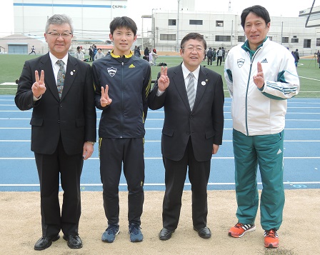 陸上部のグランドで原監督と渡邉利典さん、伊藤晃二教育長と山本市長がそれぞれピースサインをして並んで撮影した写真