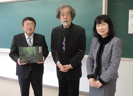 黒板の前に水越武先生と茂市久美子さんと水越先生の写真集を持った市長が並んで撮影した写真