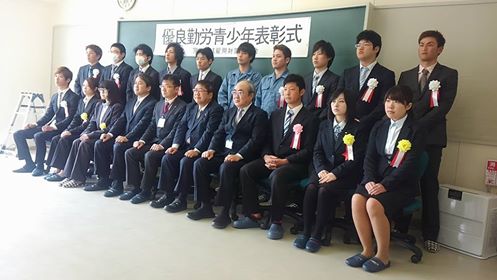 黒板に「優良勤労青少年表彰式」と書かれた横幕が貼られた前列の椅子に市長を中央に6名の受賞者と3名の関係者が座り、後列に10名の受賞者が立っている集合写真