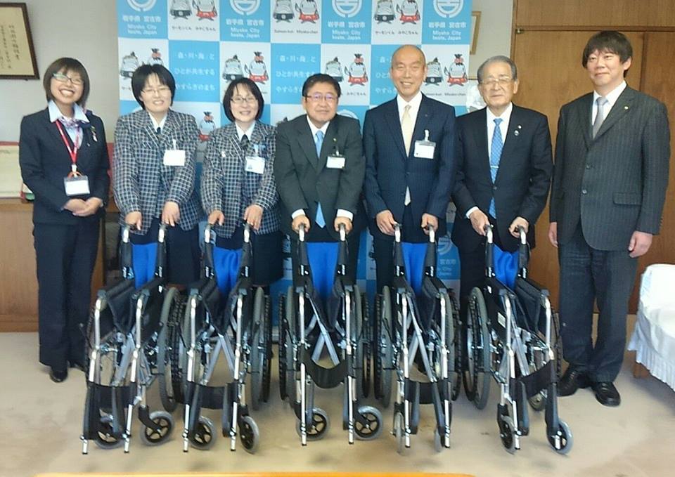 バックパネルの前で、1台ずつ寄贈いただいた車いすを持っている2名のヤクルトの女性社員や2名の関係者と市長、左側の女性と右側の男性が横一列に立っている写真