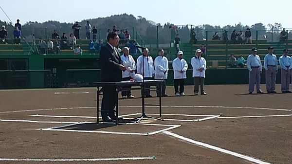 宮古市内中学校春季野球大会開会式が行われる野球場に関係者や審判が並び、一台の長机とマイクスタンドが設置されたバッターボックスで挨拶を行っている市長の写真