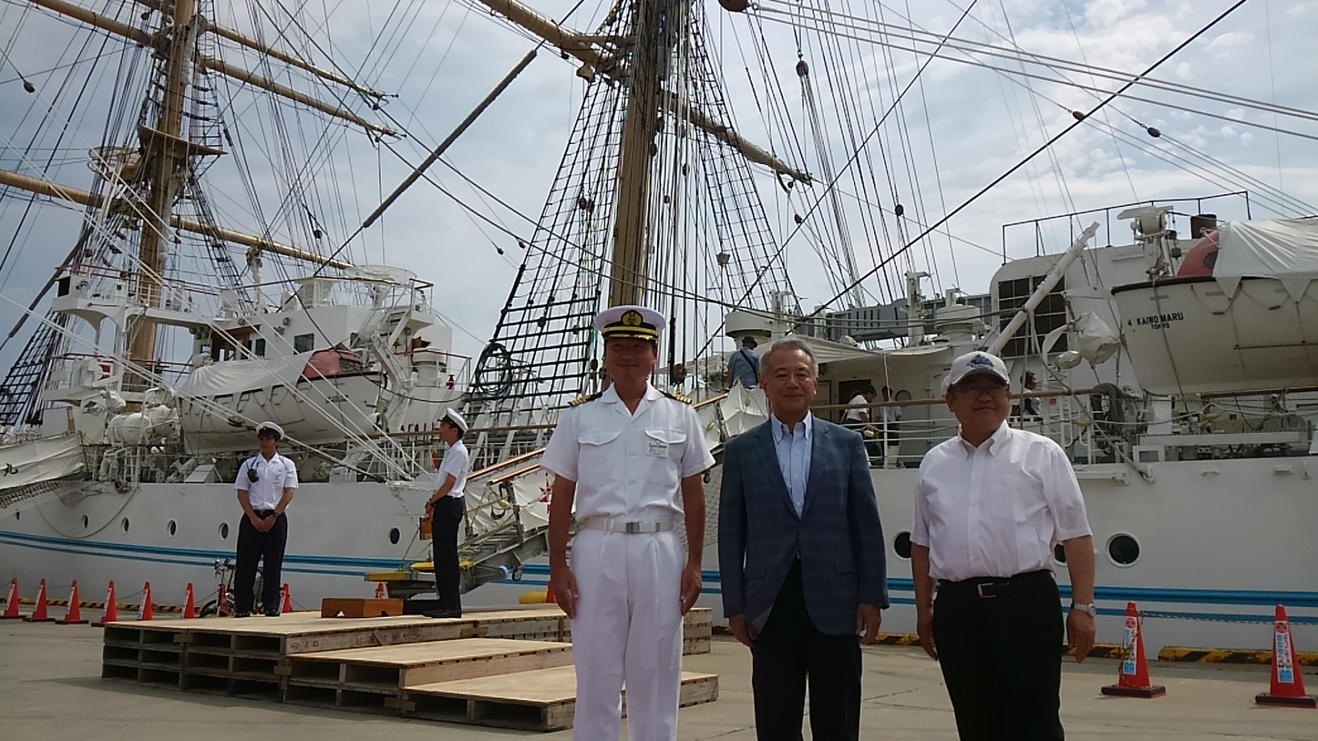 海王丸の前に立つ市長とスーツを着た男性、制帽と白い制服を着た乗組員の男性の記念写真
