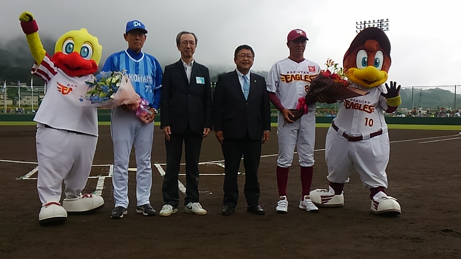 東北楽天ゴールデンイーグルスのユニフォームを着た男性、横浜DeNAベイスターズのユニフォームを着た男性、市長、スーツを着た男性、スイッチ、クラッチが並んでいる記念写真
