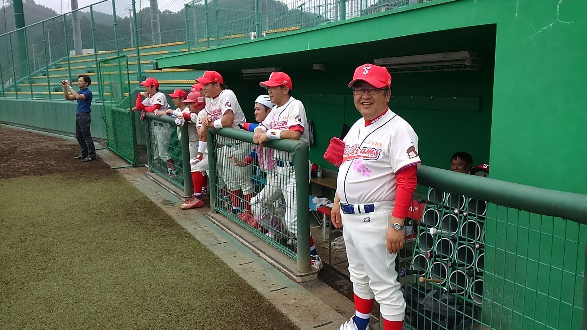野球場のダッグアウトから柵に体を乗り出して、球場の方を見る選手や市長の写真