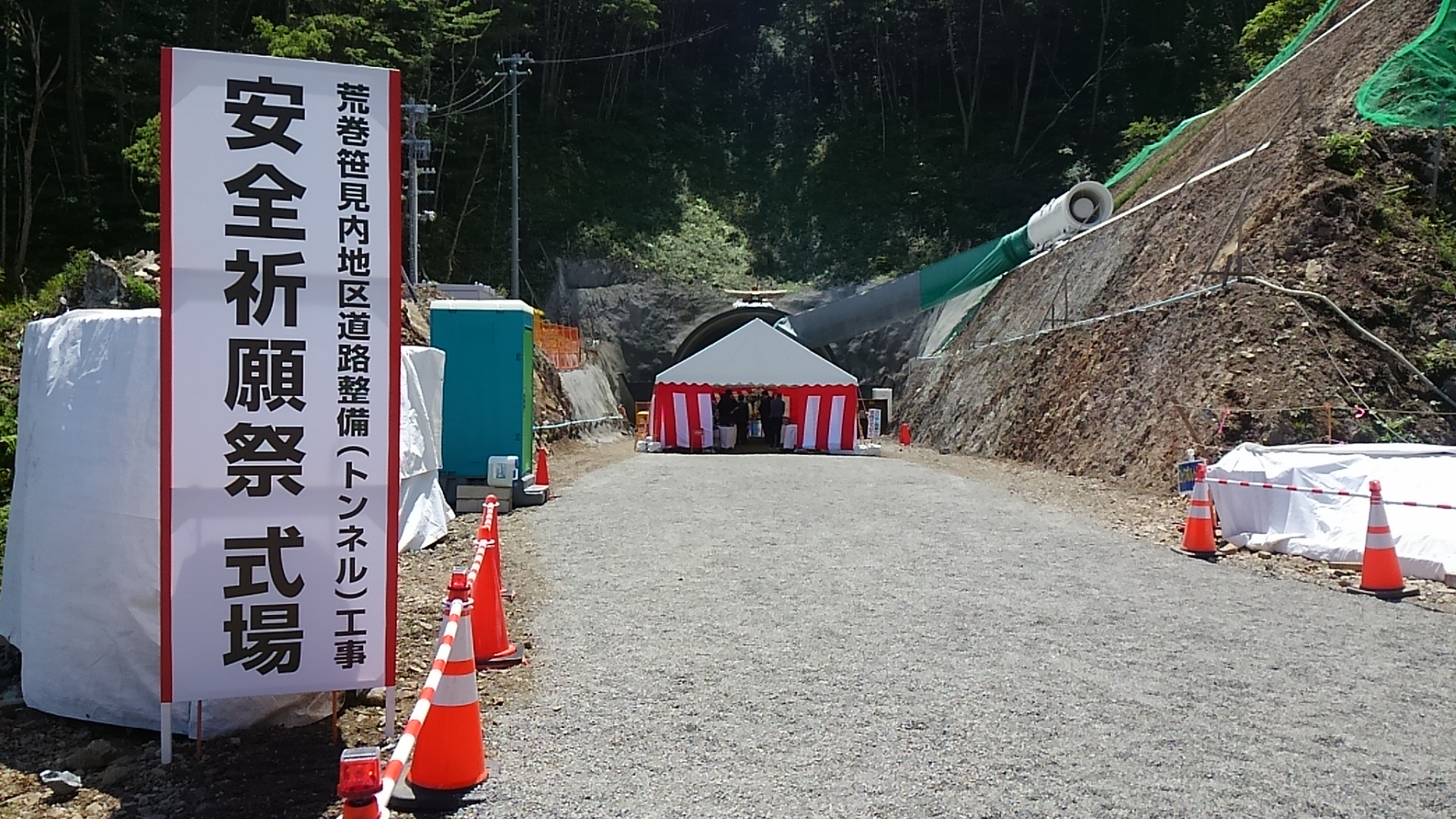 道の脇に「安全祈願祭 式場」と書かれた看板が立てられ、道の先に紅白幕が張られたテントが設置してある様子の写真