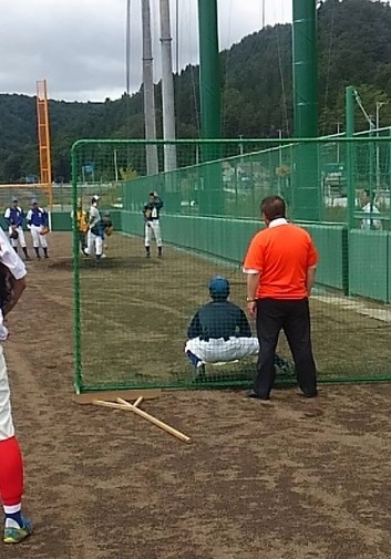 ピッチング練習をする選手たちの後ろで、ネット越しに眺める市長の写真