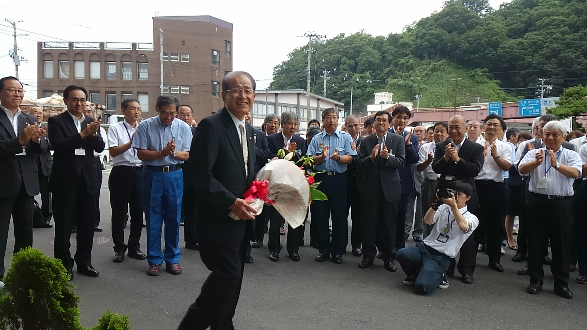 並んで拍手をする大勢の職員の方々の前を花束を持って歩く山口公正副市長の写真