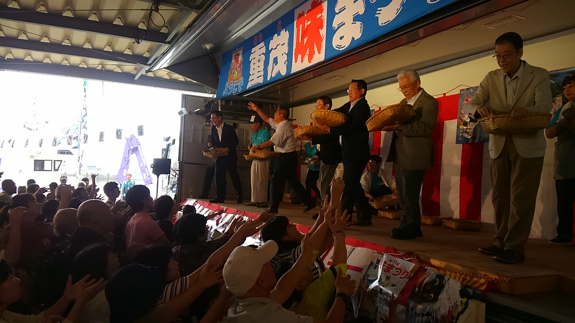 ウィングトラックの荷台から餅まきをしている様子の市長と関係者の男性たちと、下で両手を大きく伸ばしている参加者たちの写真