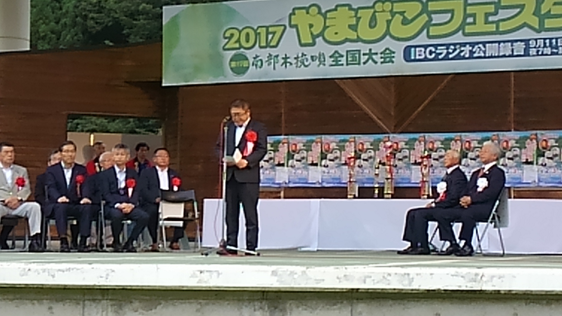 「2017やまびこフェスタ」と書かれた大きな横断幕が掲げられたステージ左右に胸章リボンを付けた来賓者が座り、中央のマイクスタンドの前で挨拶を行っている市長の写真