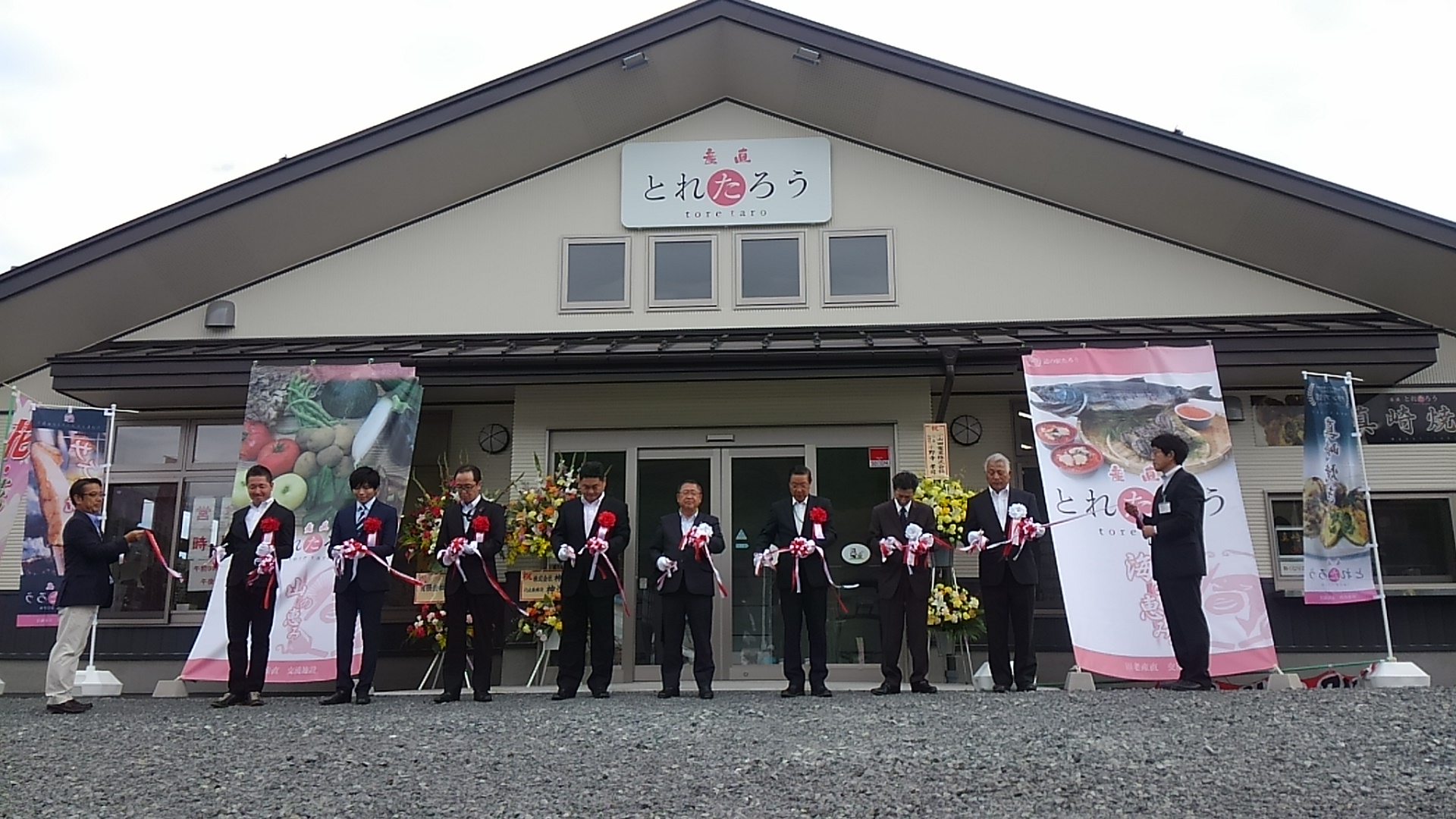 田老地区産直・交流施設「とれたろう」の建物の前で、8名の関係者が横一列に並びテープカットが行われている様子の写真