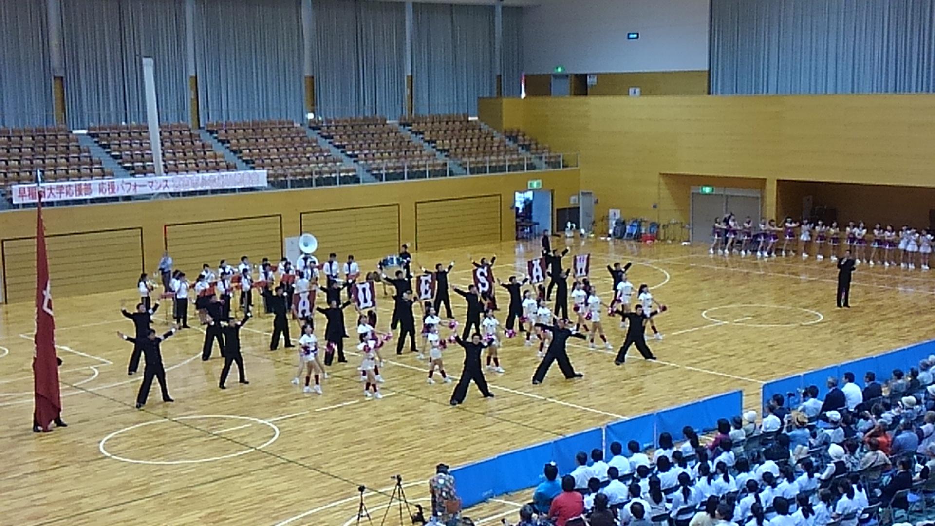 沢山の観客が集まった体育館で、早稲田大学応援部の吹奏楽部がマーチングを行うなか、チアリーダーや応援団がパフォーマンスを披露している「宮古市ふれあい発表会」の様子の写真