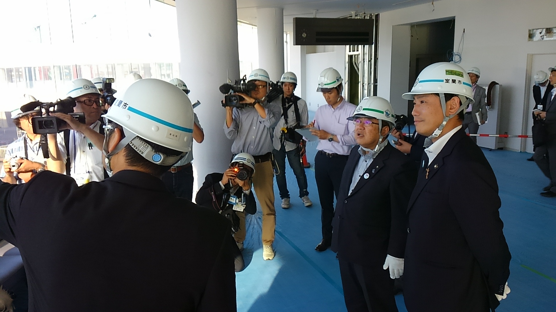 周囲にテレビ局のカメラで撮影されているなか、ヘルメットを被った室蘭市の青山市長と市長が室蘭フェリーターミナルの改修工事を視察している様子の写真