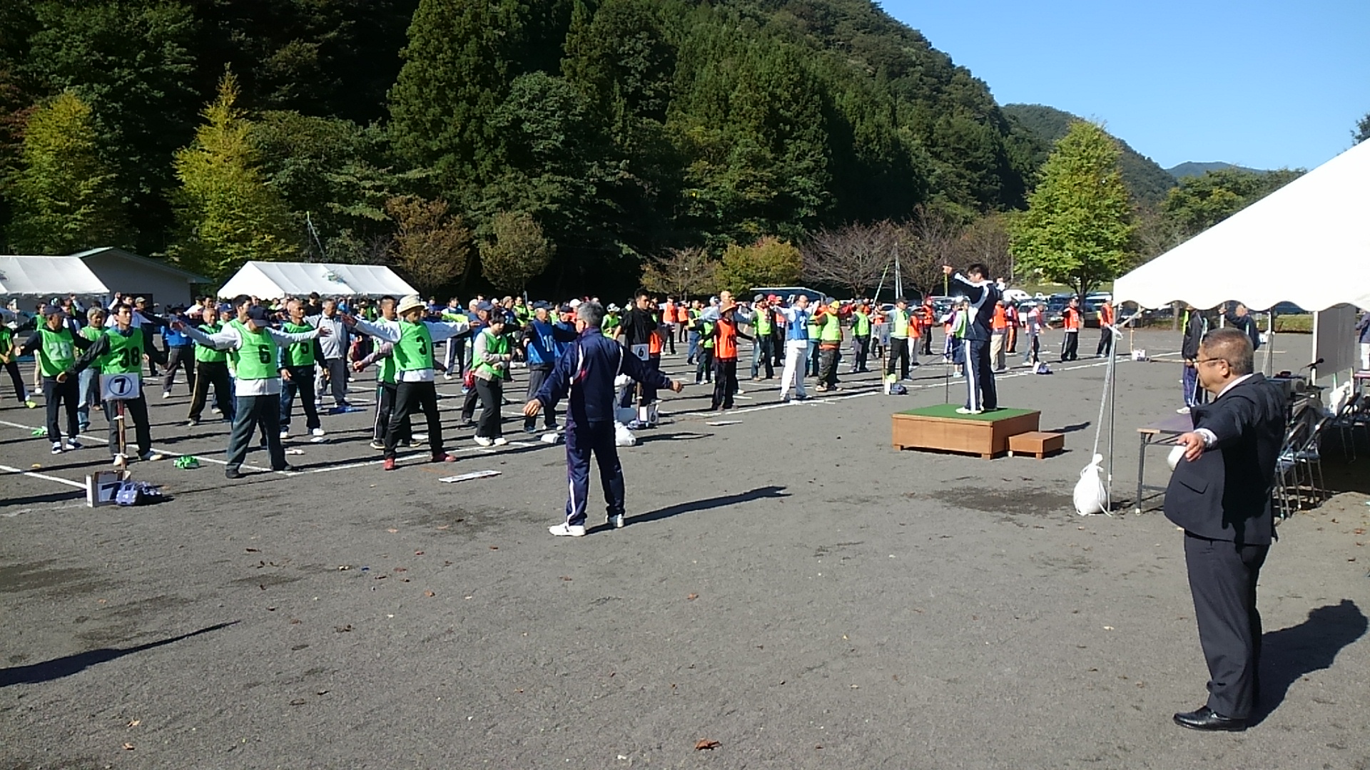 緑色やオレンジ色のゼッケンを着た大勢の参加者の方々が、グラウンドに広がって両手を横に大きく広げている写真