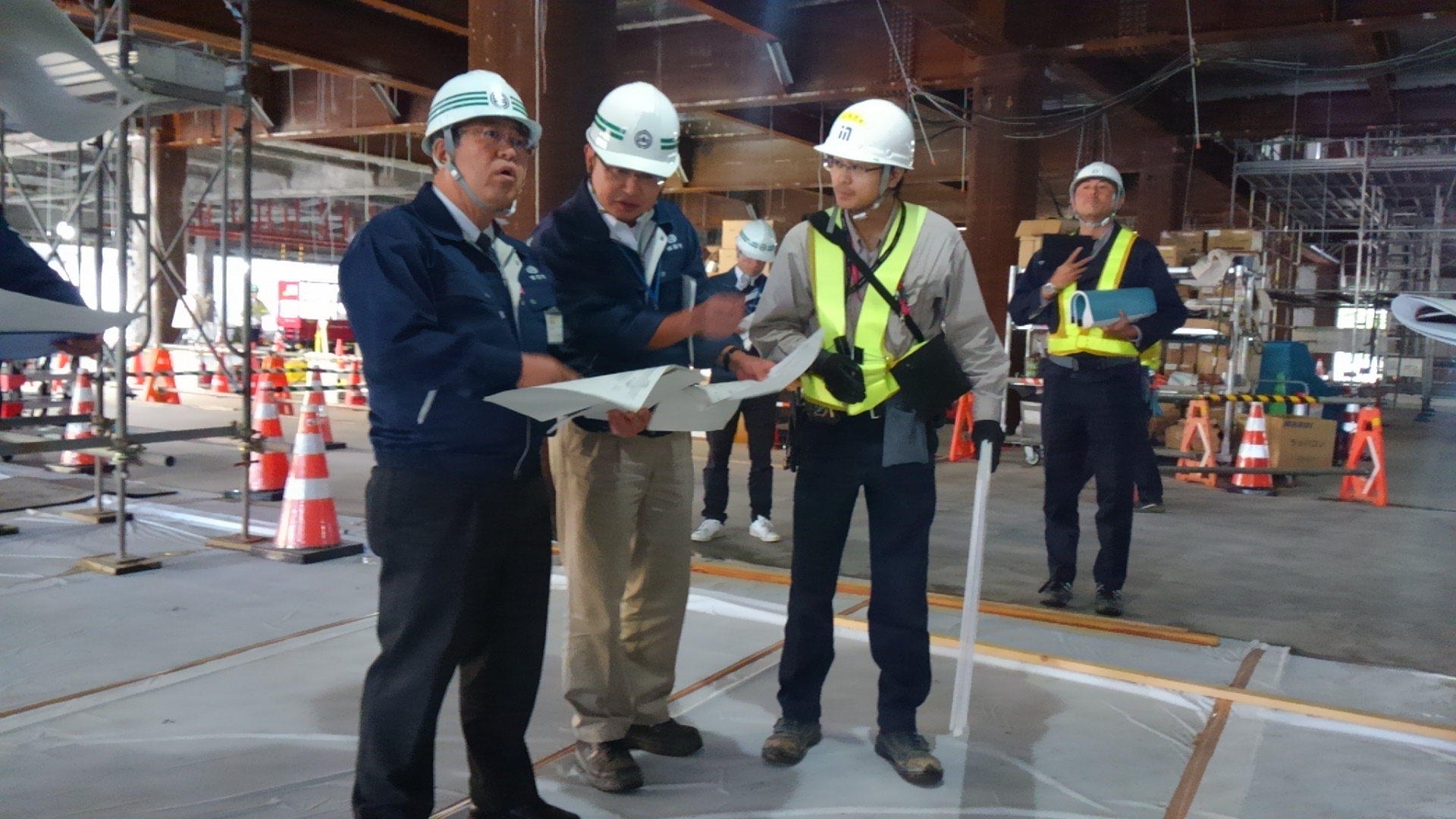 建設中の鉄骨の建物の下で、ヘルメットを被り資料を広げて話をしている様子の市長と2名の男性の写真