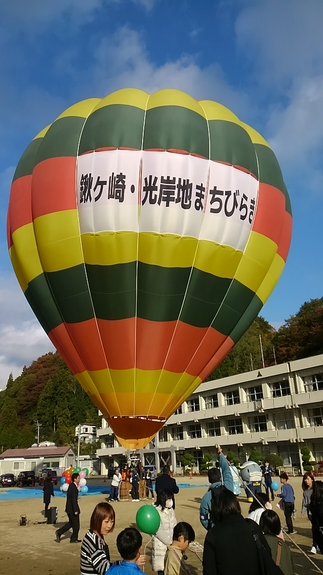 「鍬ヶ崎・光岸地まちびらき」と書かれた黄色・緑色・オレンジ色のデザインの気球が膨らんでいる様子の写真