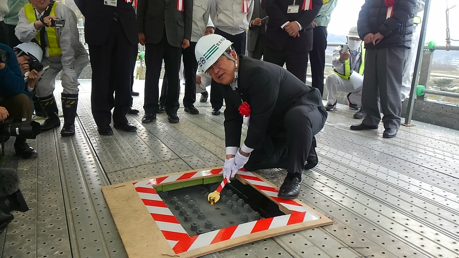 ヘルメットを被り白い手袋を着けた市長が、足元にあるボルトをナットで締めている写真