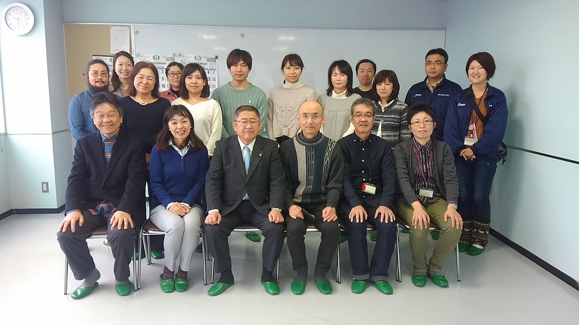 椅子に座る市長と5名の男女の後方で、12名の男女が立って並んでいる記念写真