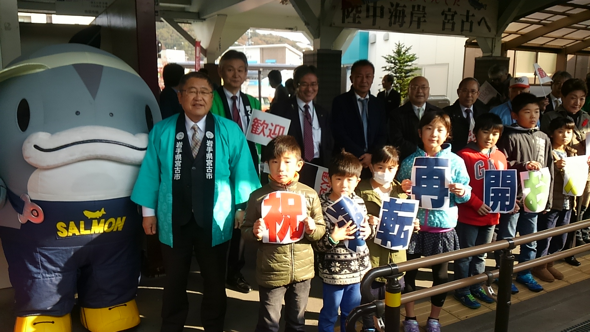 青い法被を着た市長と子供たち、サーモンくんが並んでいる写真