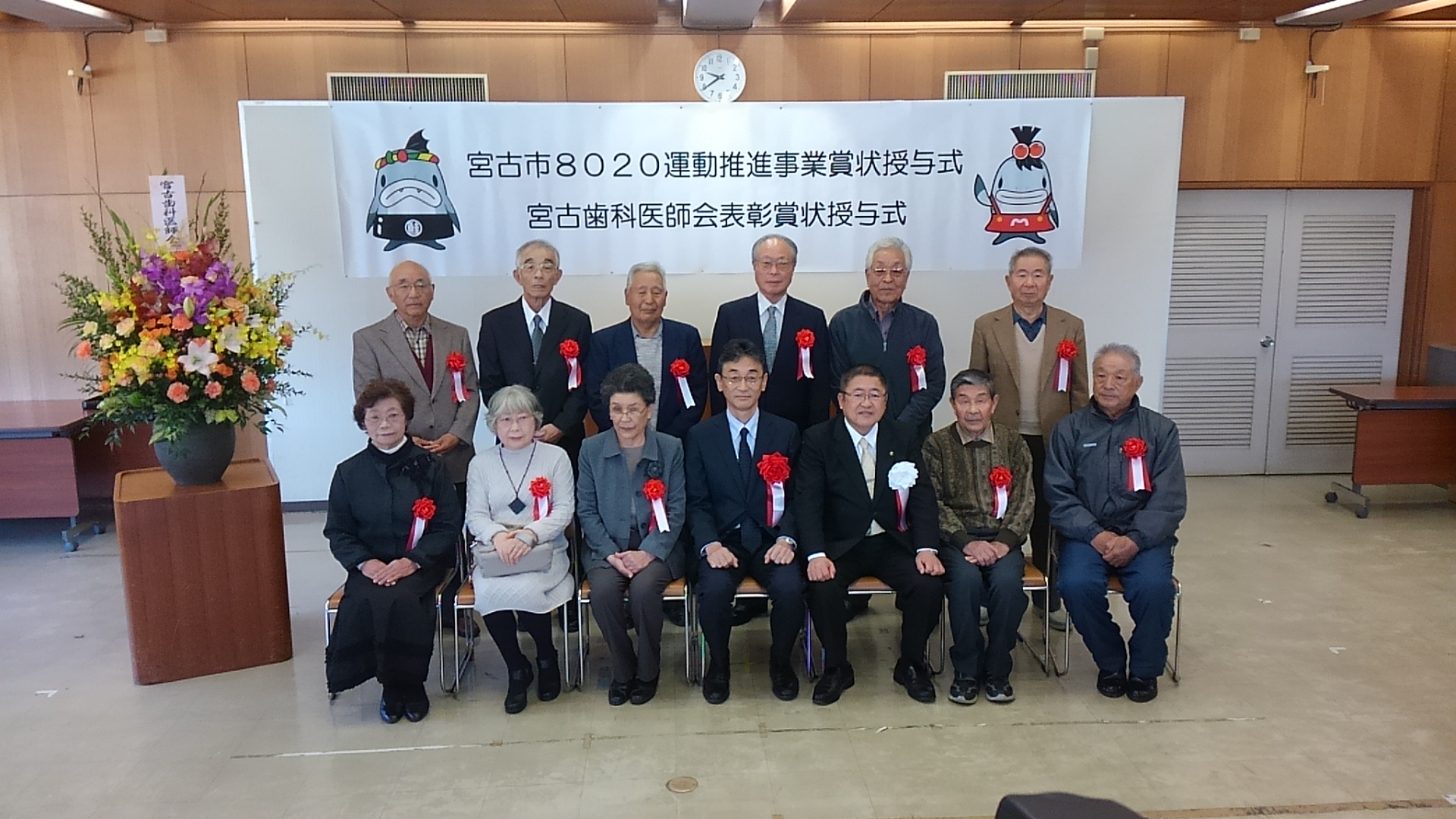 市長と3名の男性、3名の女性が椅子に座り、後列で6名の男性が立って並んでいる記念写真