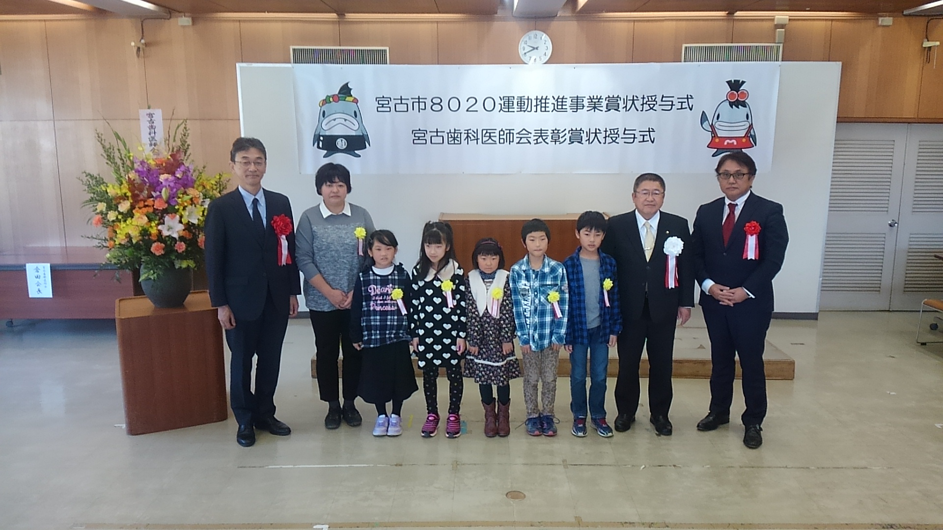 5名の子供と、女性1名、市長を含む3名の男性が横一列に並んでいる記念写真