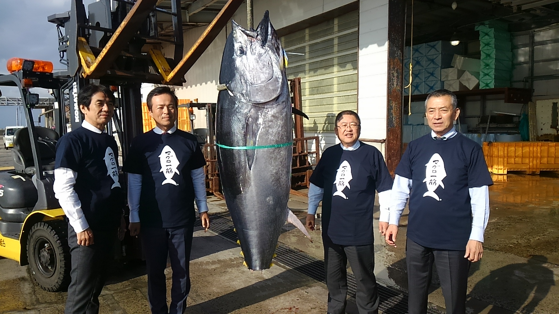 吊るされたマグロの両側に立つ市長と3名の男性の写真