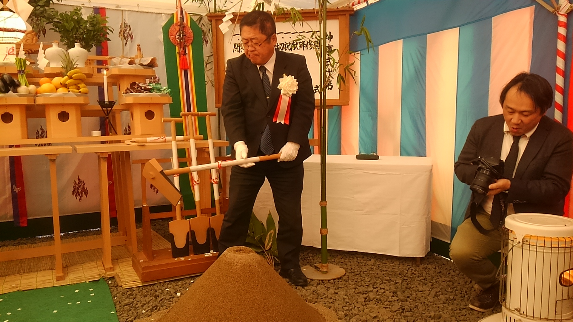 スーツを着て白い手袋を着けた市長が盛り土に鍬入れをしようとしている写真