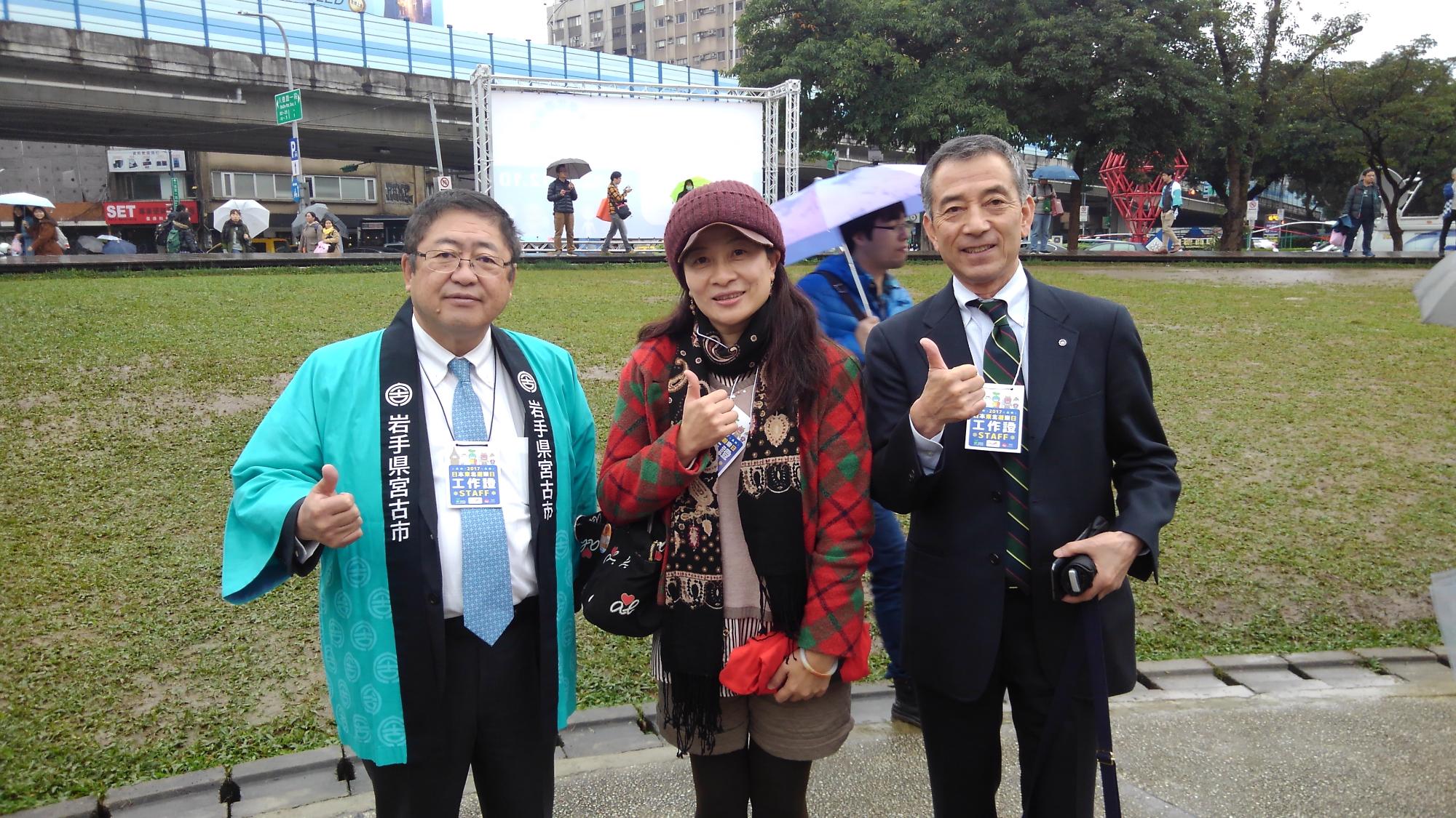 右手の親指を上にあげたポーズをとる市長と女性1名、男性1名の記念写真