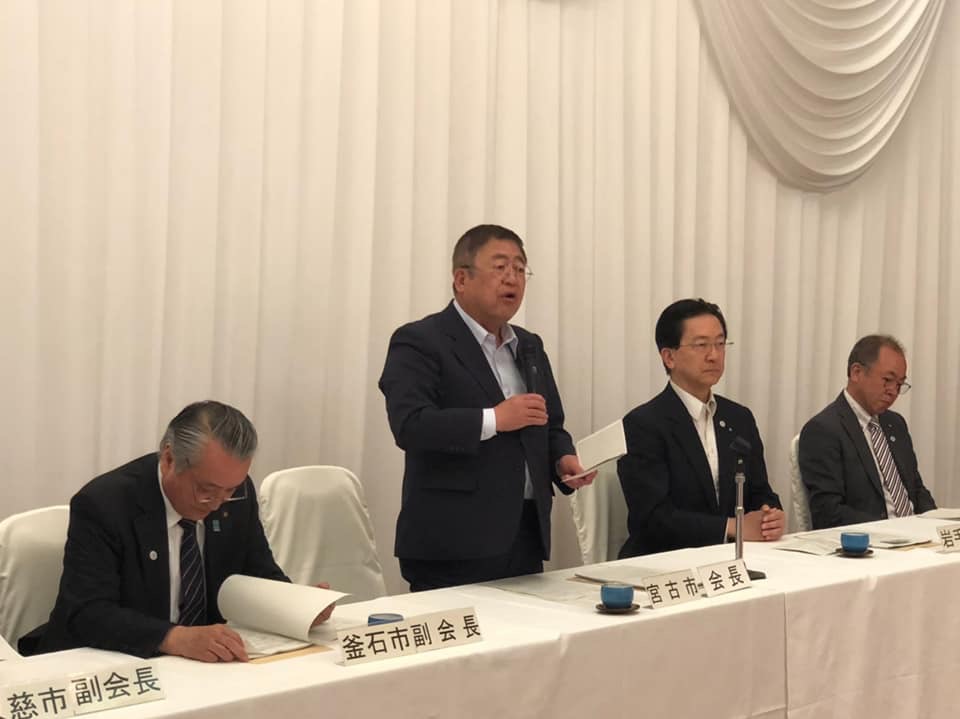 達増知事や市町村の代表者が座っている「三陸ジオパーク推進協議会総会」の席で、自席から立ち上がり右手にマイクを持って話をしている市長の写真